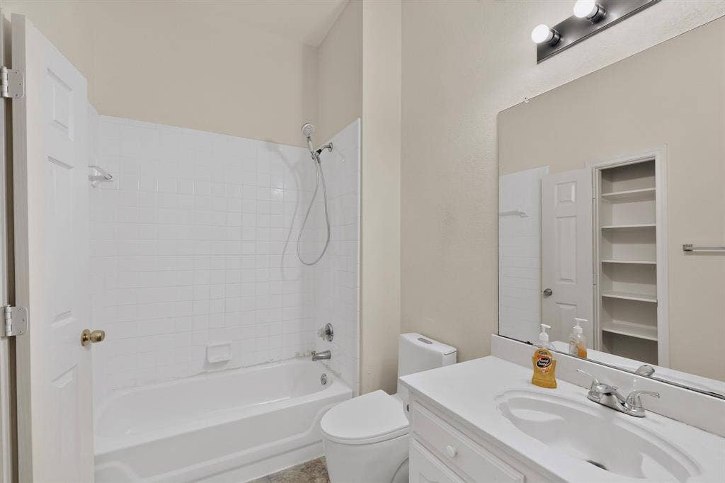 8108 Case Drive, Plano, TX 75025 White tile shower surround, bathtub with shower fixture, single vanity with integrated sink, wall-mounted mirror, and built-in shelving