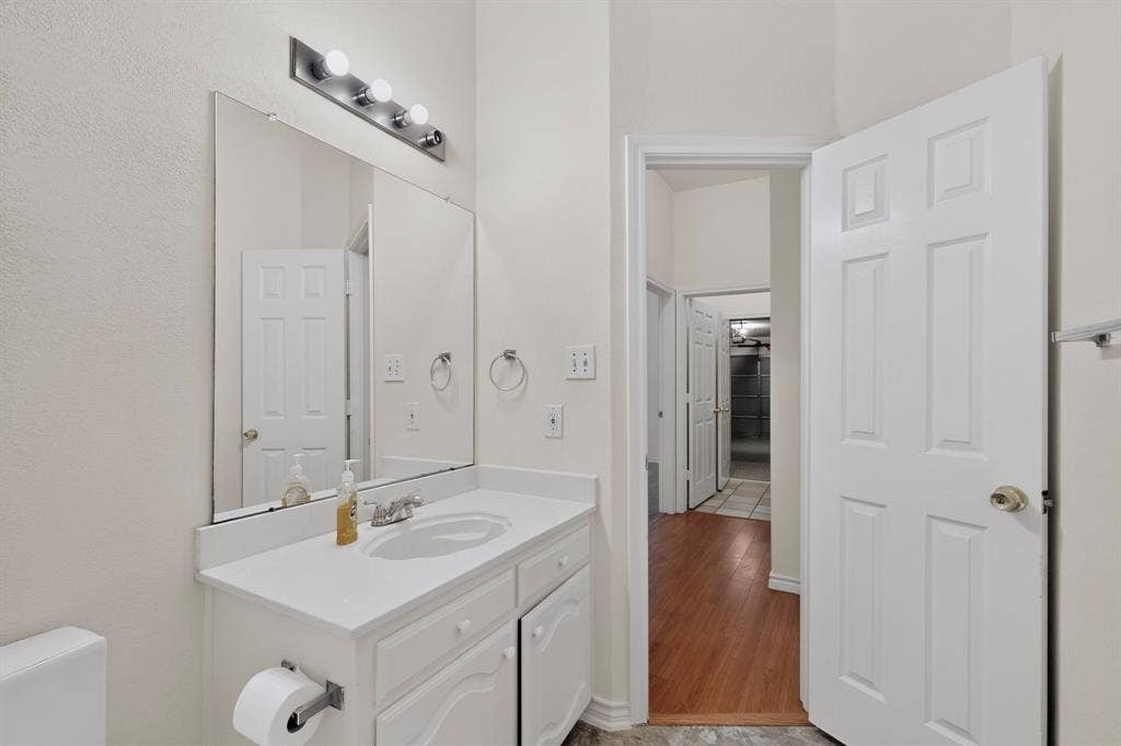 8108 Case Drive, Plano, TX 75025 White vanity with an integrated sink and chrome faucet, illuminated by a four-bulb vanity light, with wood-finish flooring extending from the doorway