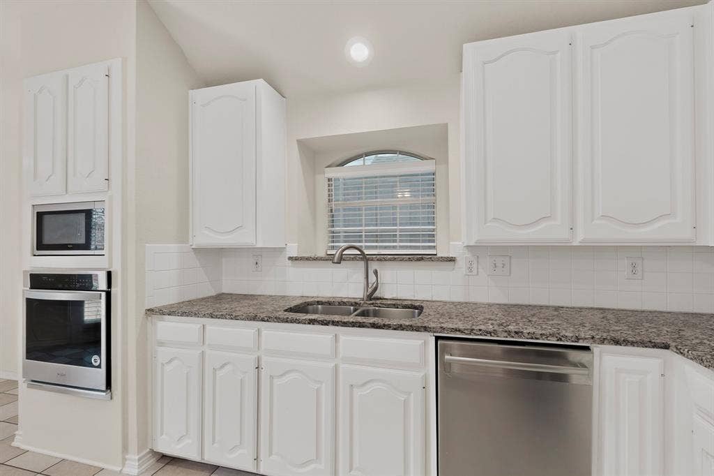 8108 Case Drive, Plano, TX 75025 White cabinetry with arch details, stainless steel double basin sink, stainless steel dishwasher, speckled countertops, and white tile backsplash