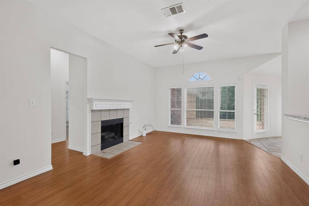 8108 Case Drive, Plano, TX 75025 High vaulted ceiling with a ceiling fan, wood-finish flooring, tiled fireplace with a mantel, large windows with an arched transom, and a glass-paneled exterior door