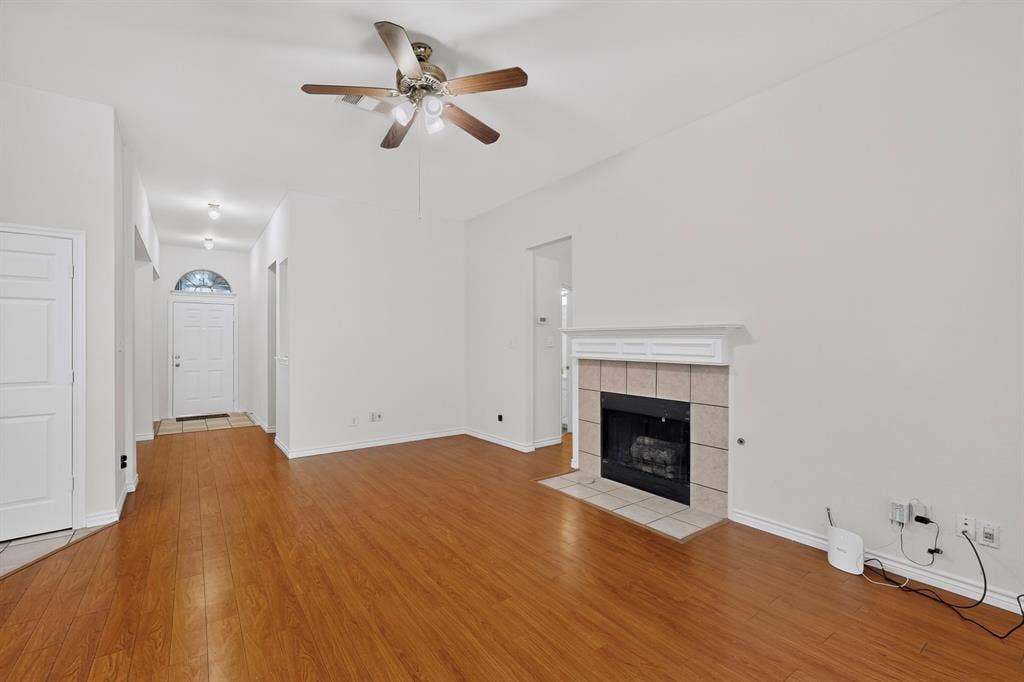 8108 Case Drive, Plano, TX 75025 Vaulted ceiling with a ceiling fan, fireplace with a tile surround and mantel, wood-finish flooring, and an arched transom window above the entry door