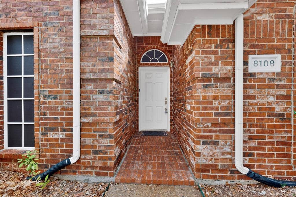8108 Case Drive, Plano, TX 75025 Brick exterior with white trim, arched window above the entry door, and a brick-paved entryway
