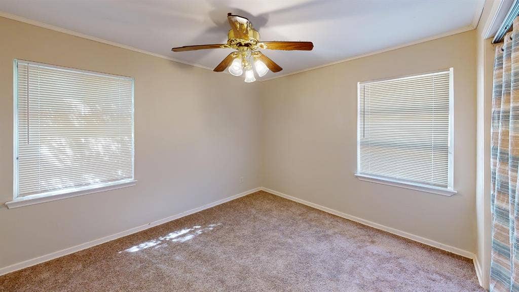 Neutral wall tones, carpet flooring, two windows with blinds, and a ceiling fan with integrated lighting