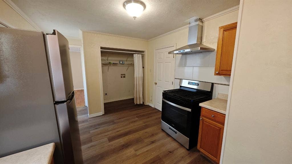 Kitchen featuring wood-finish flooring, stainless steel appliances, wood cabinetry, and a tile backsplash