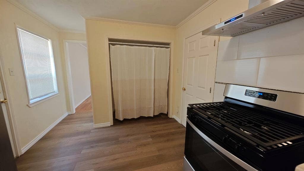 Wood-finish flooring, white trim, stainless steel range hood, white subway tile backsplash, and a gas range