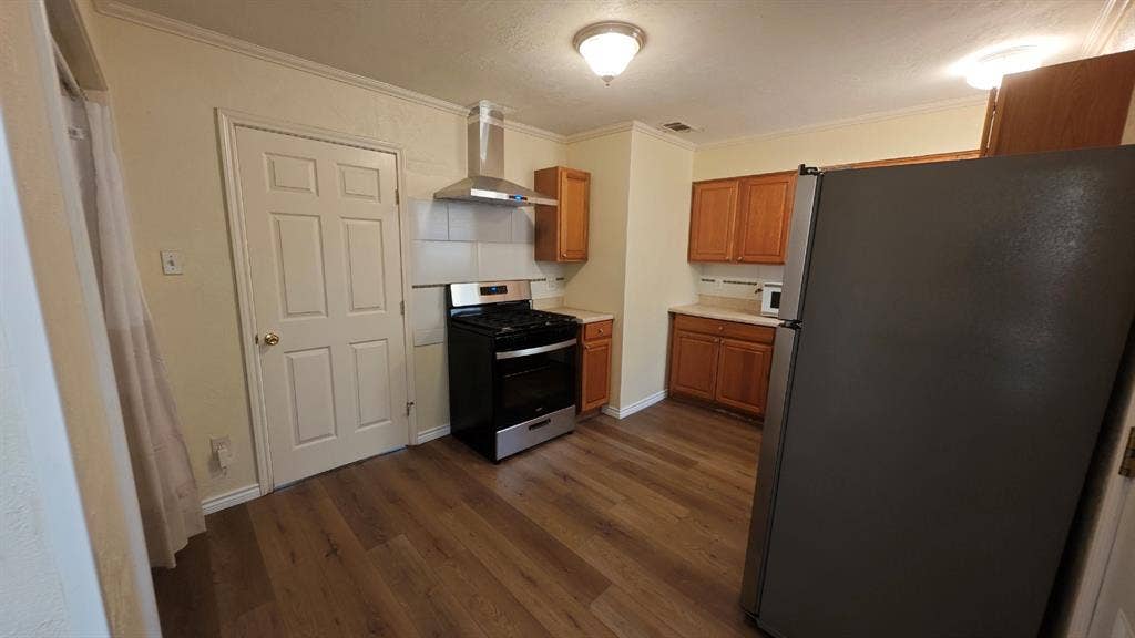 Kitchen featuring wood-finish flooring, wood cabinetry, a stainless steel range hood, and a built-in range
