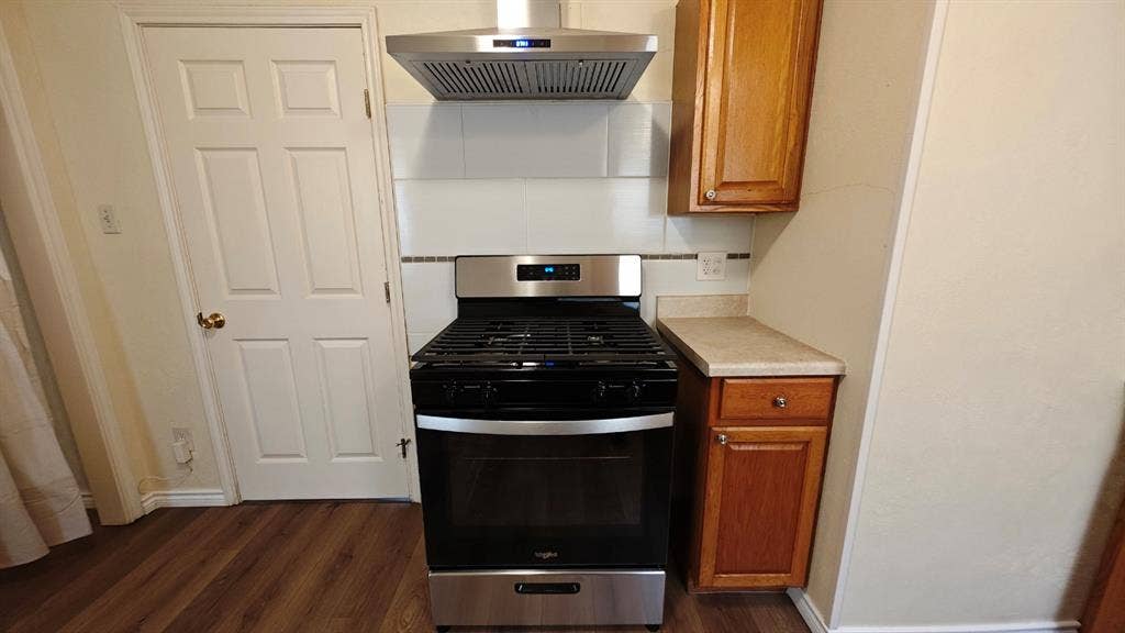 Stainless steel range with a coordinating hood, wood-finish flooring, and light-toned cabinetry
