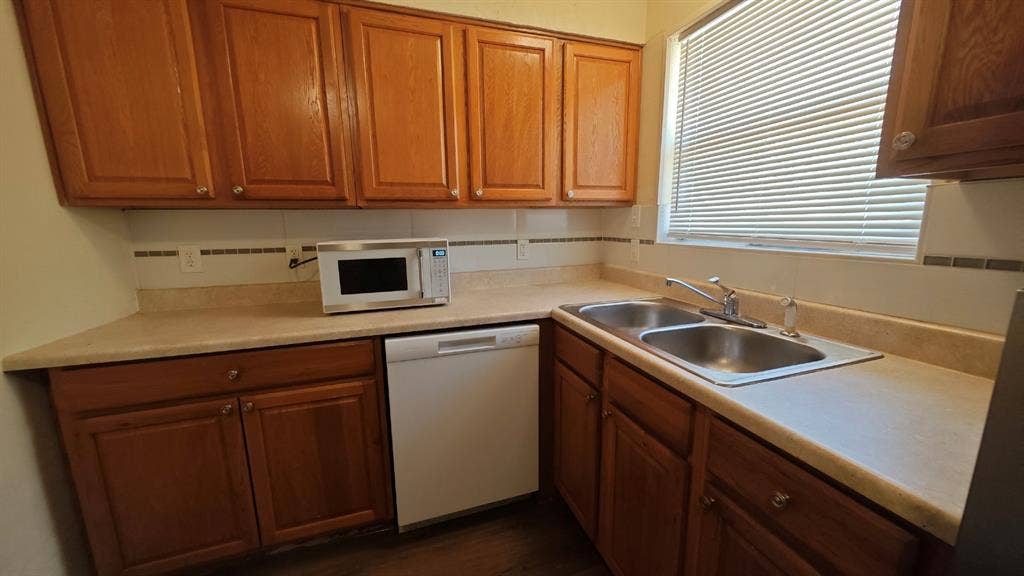 Wood-finish cabinetry, light-toned countertops, and a stainless steel double basin sink with a chrome faucet