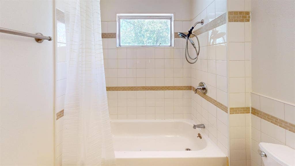 Bathtub with a shower/tub combination, white wall tiling, decorative accent tiling, and a window