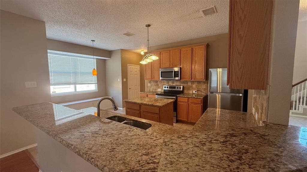 1433 Winterwood Drive, Allen, TX 75002 Kitchen featuring granite countertops, wood cabinetry, stainless steel appliances, and a breakfast bar with a double basin sink