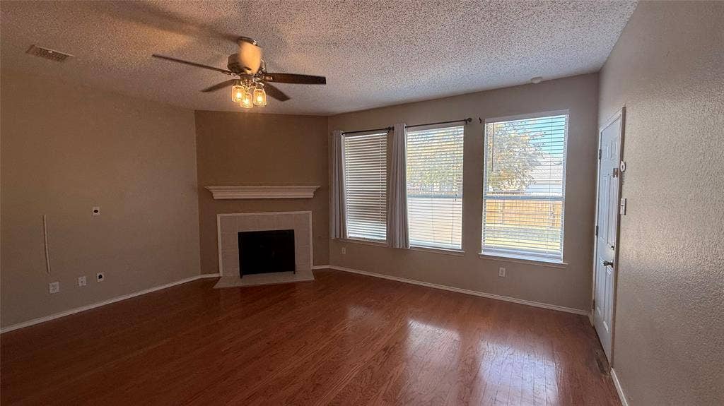 1433 Winterwood Drive, Allen, TX 75002 Spacious room featuring wood-finish flooring, a ceiling fan with integrated lighting, and a corner fireplace with a white mantel and tile surround