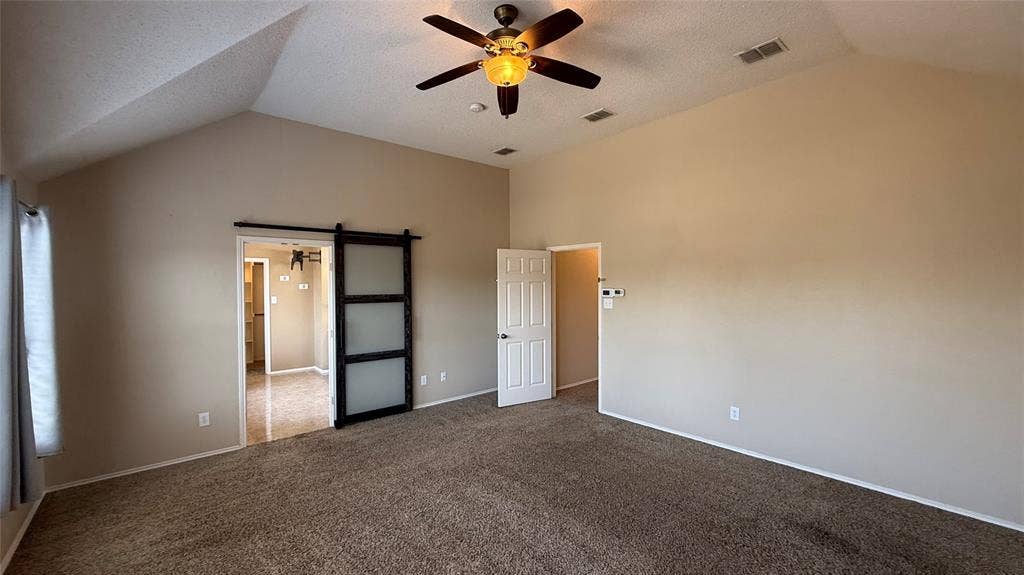 1433 Winterwood Drive, Allen, TX 75002 Vaulted ceiling with a ceiling fan, carpeted flooring, and a sliding barn door with frosted glass panels