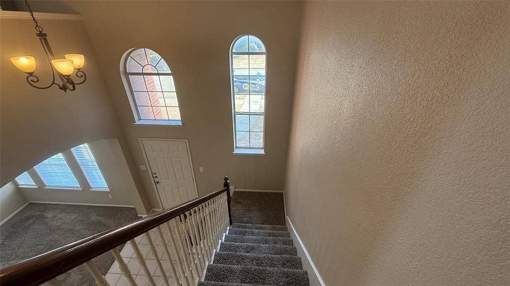 1433 Winterwood Drive, Allen, TX 75002 Two-story entry featuring arched windows, a chandelier, and a carpeted staircase with a wood handrail