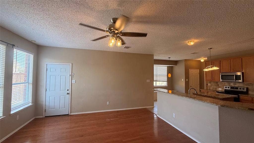 1433 Winterwood Drive, Allen, TX 75002 Wood-finish flooring, ceiling fan with integrated lighting, kitchen featuring wood cabinetry, stainless steel appliances, and a stone-finish countertop