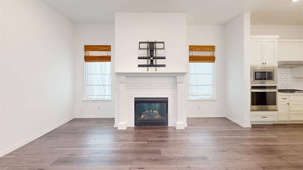 3285 Dover Drive, McKinney, TX 75069 Hardwood-finish flooring throughout, featuring a fireplace with white subway tile surround and mantle, and built-in stainless steel oven and microwave