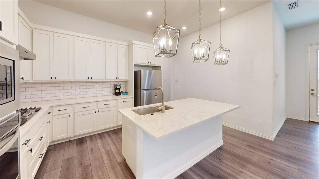 3285 Dover Drive, McKinney, TX 75069 Kitchen featuring white cabinetry, subway tile backsplash, stainless steel appliances, wood-finish flooring, and a center island with pendant lighting