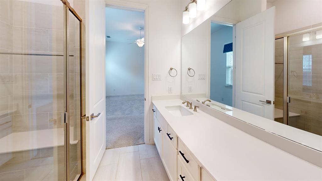 3285 Dover Drive, McKinney, TX 75069 Dual vanity with undermount sinks and wall-mounted faucets, large mirror, walk-in shower with glass enclosure, tiled walls, and built-in bench