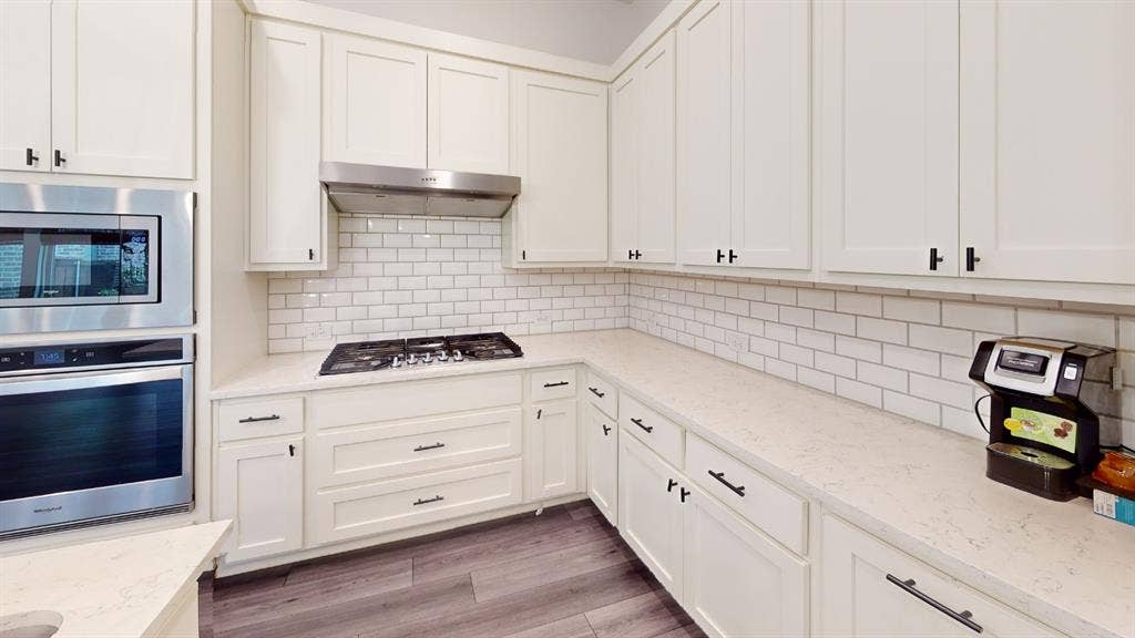 3285 Dover Drive, McKinney, TX 75069 White shaker cabinetry with matte black hardware, stainless steel built-in microwave and oven, gas cooktop, white subway tile backsplash, and light-toned countertops