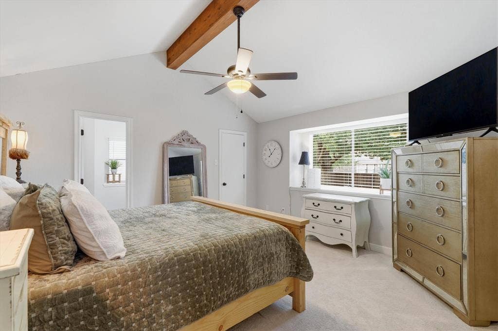 Spacious primary suite features a vaulted ceiling, exposed wood beam and large window providing abundant natural light.