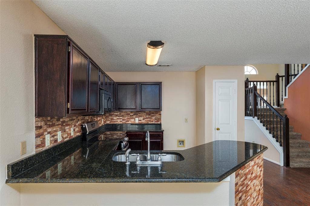 4500 Fargo Drive, Grand Prairie, TX 75052 Kitchen featuring dark wood-finish cabinetry, a stone-tile backsplash, and a dark stone-finish countertop with an integrated sink