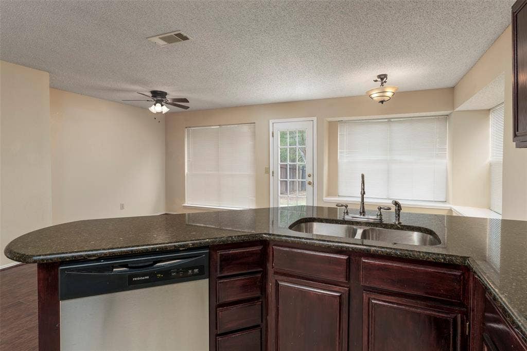 4500 Fargo Drive, Grand Prairie, TX 75052 Kitchen island with a dark countertop, stainless steel dishwasher, and dark wood cabinetry