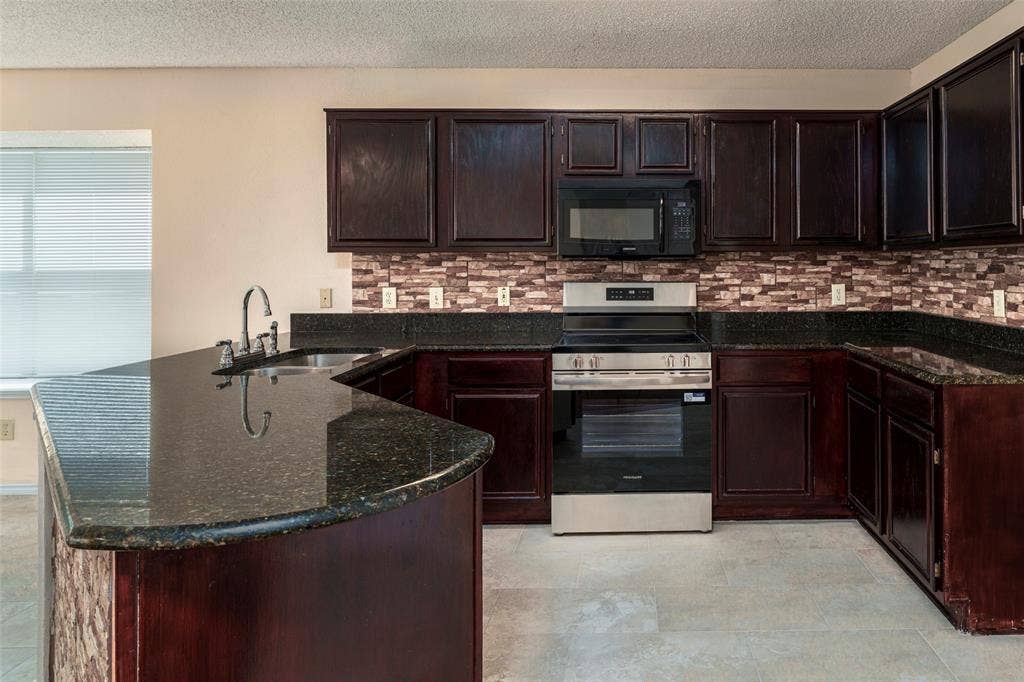 4500 Fargo Drive, Grand Prairie, TX 75052 Kitchen with dark cabinetry, stone countertops, stainless steel appliances, a tile backsplash, and light-colored flooring