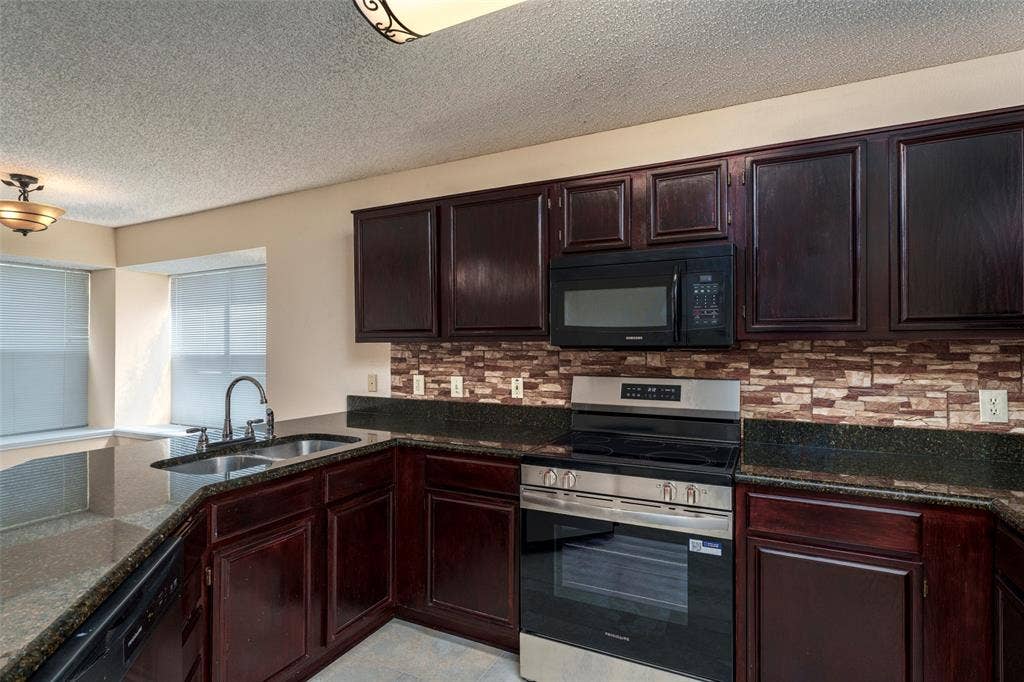 4500 Fargo Drive, Grand Prairie, TX 75052 Kitchen featuring dark wood cabinetry, a mosaic tile backsplash, dark countertops, a stainless steel range, and an integrated microwave