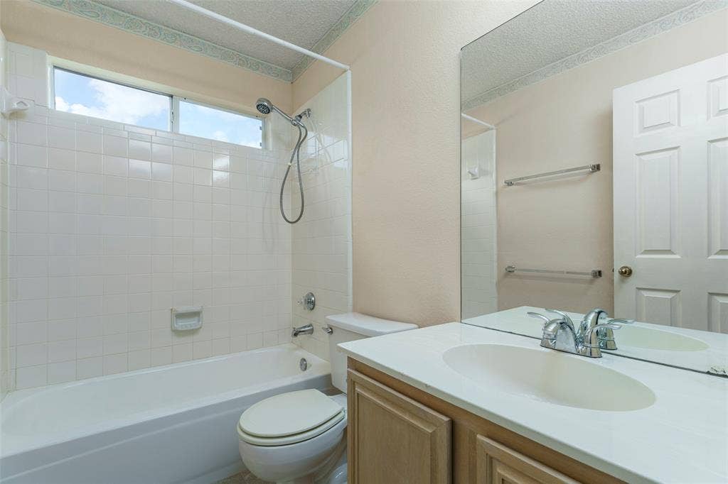 4500 Fargo Drive, Grand Prairie, TX 75052 White tiled bathtub and shower combination with an overhead window, a vanity with an integrated sink, and an expansive wall mirror