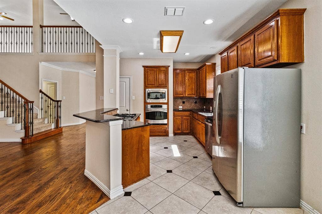 4908 Rushden Road, McKinney, TX 75070 Kitchen with wood-finish cabinetry, stainless steel appliances, and a black countertop island
