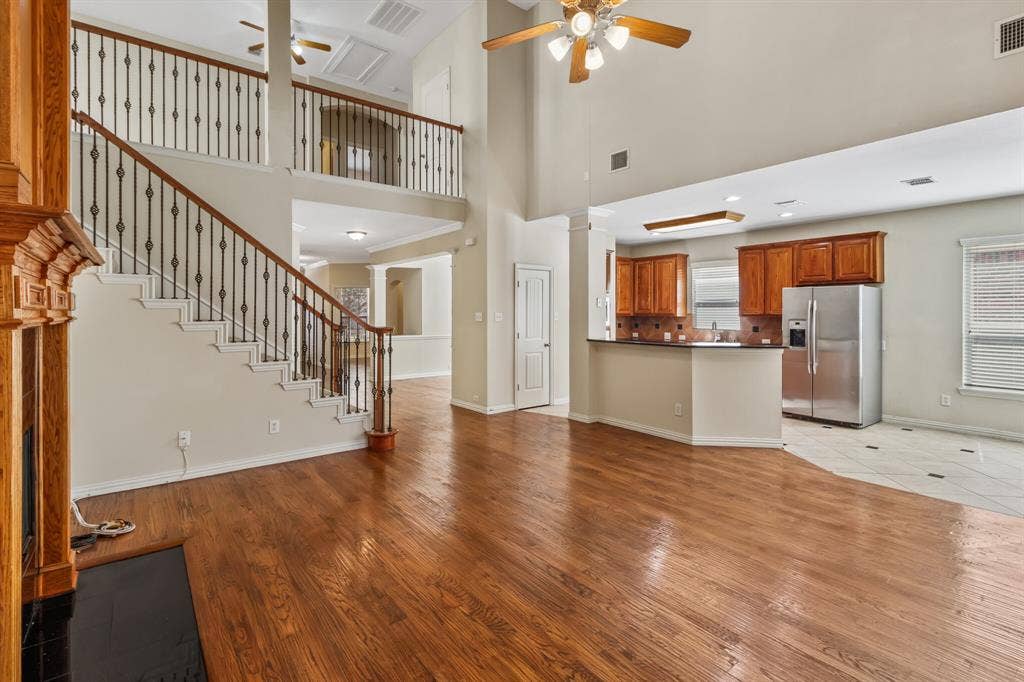 4908 Rushden Road, McKinney, TX 75070 Two-story living area featuring wood-finish flooring, a grand staircase with wrought iron balusters, a kitchen with wood cabinetry, and a ceiling fan