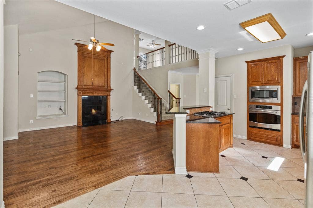 4908 Rushden Road, McKinney, TX 75070 Vaulted ceiling with ceiling fan, wood-finish flooring, built-in fireplace with wood mantel, kitchen with built-in stainless steel appliances, and a tiled kitchen floor