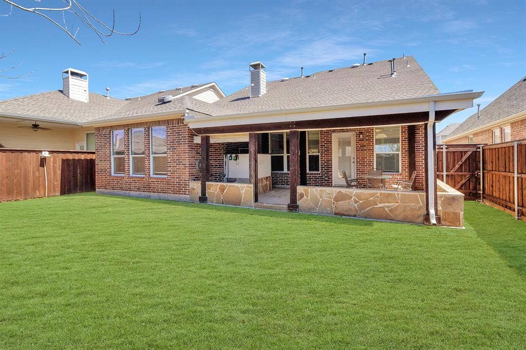 4908 Rushden Road, McKinney, TX 75070 Expansive backyard with a covered patio featuring stone-clad supports, a brick exterior, and a wood privacy fence