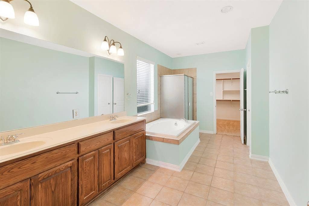 4908 Rushden Road, McKinney, TX 75070 Dual wood-finish vanity with integrated sinks, built-in soaking tub, tiled shower enclosure, and tiled flooring