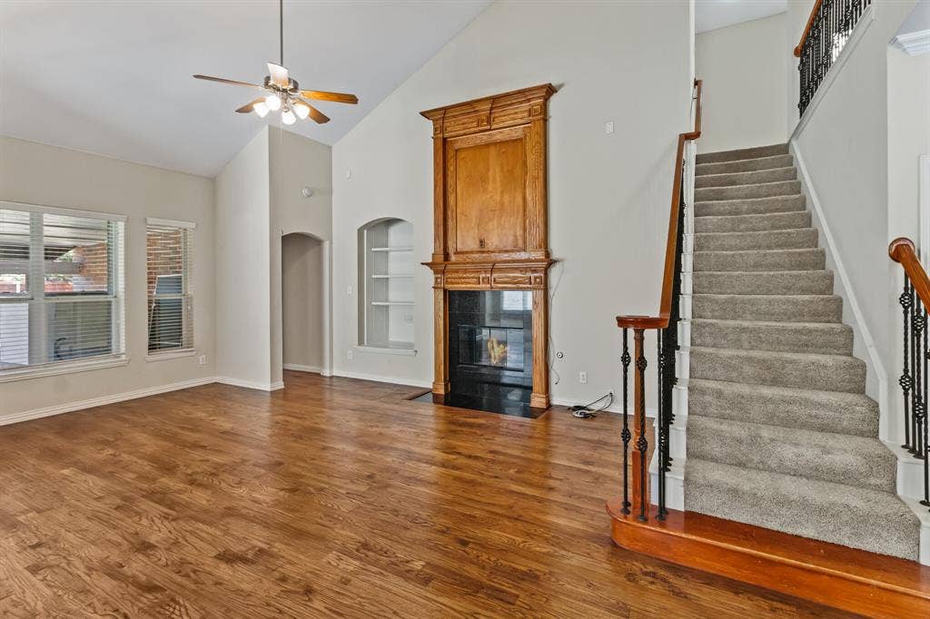 4908 Rushden Road, McKinney, TX 75070 Vaulted ceiling with ceiling fan, wood-finish flooring, built-in fireplace with wood mantel, built-in shelving, carpeted staircase with wrought iron balusters