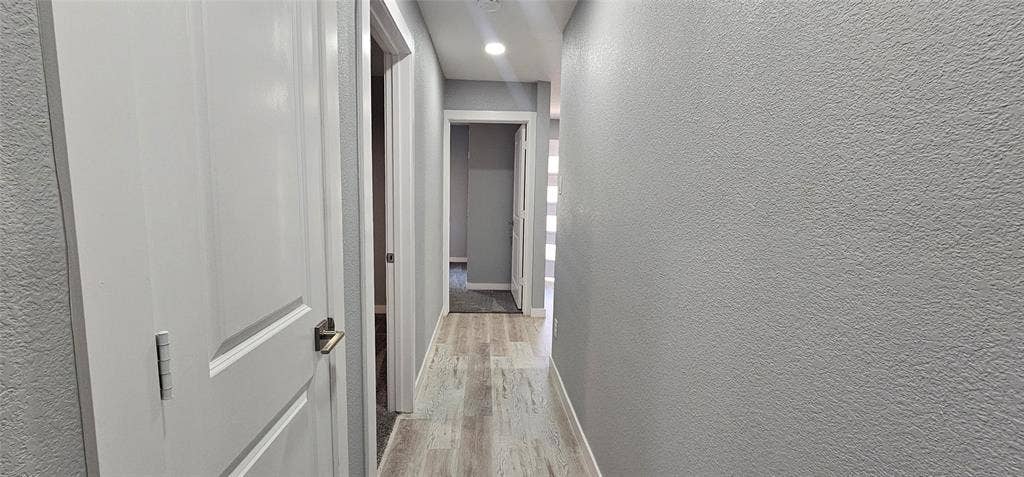Hallway featuring wood-finish flooring, recessed lighting, and panel doors with lever hardware