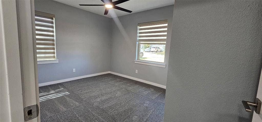 Carpeted flooring, neutral wall tones, two windows with horizontal blinds, and a ceiling fan with integrated lighting