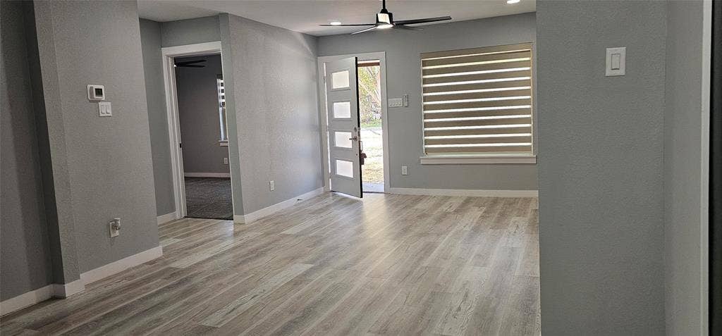 Light-toned wood-finish flooring, recessed lighting, ceiling fan, and modern entry door with frosted glass panels