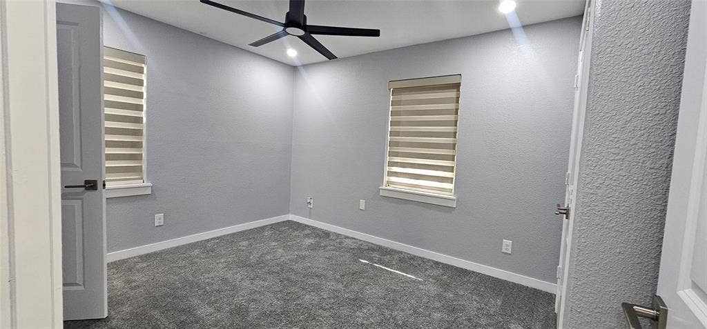 Modern ceiling fan with integrated lighting, recessed ceiling lighting, textured walls, two windows with horizontal blinds, and grey carpeting