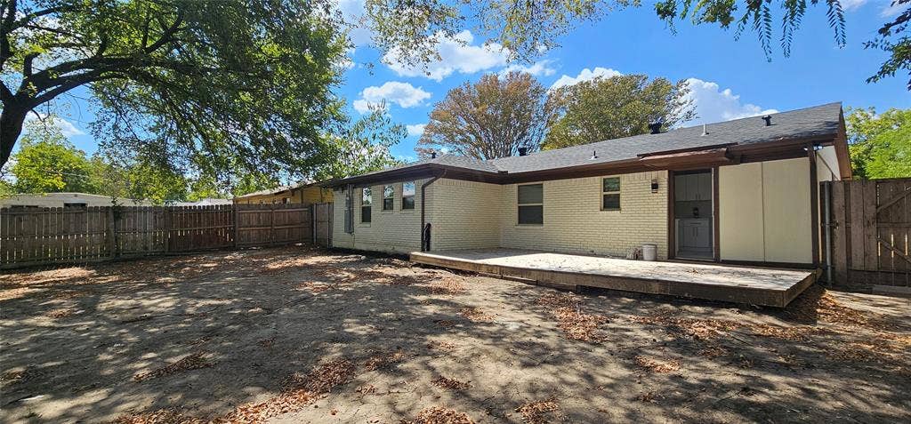 Expansive backyard featuring a wood privacy fence, a raised wood deck, and mature trees providing shade