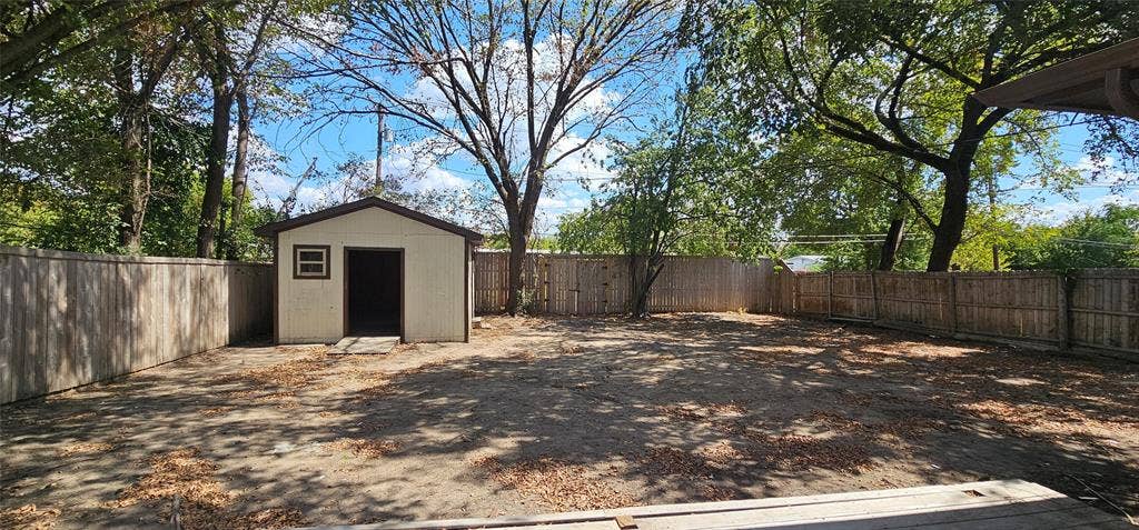 Expansive yard featuring a privacy fence, mature trees, and an exterior storage shed with a window