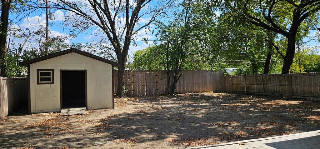 Expansive outdoor area featuring a storage shed, wood fencing, and mature trees