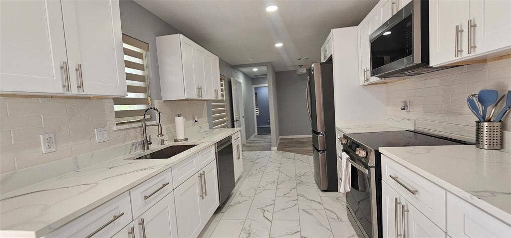 Kitchen featuring white cabinetry, light-toned countertops, stainless steel appliances, a tile backsplash, and patterned tile flooring