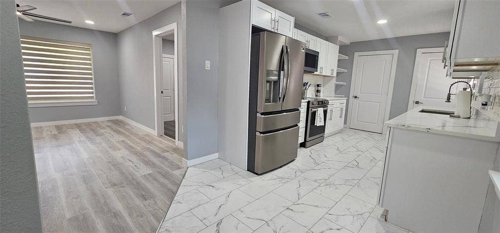 Modern kitchen with white cabinetry, stainless steel appliances, marble-look tile flooring, and light-toned countertops