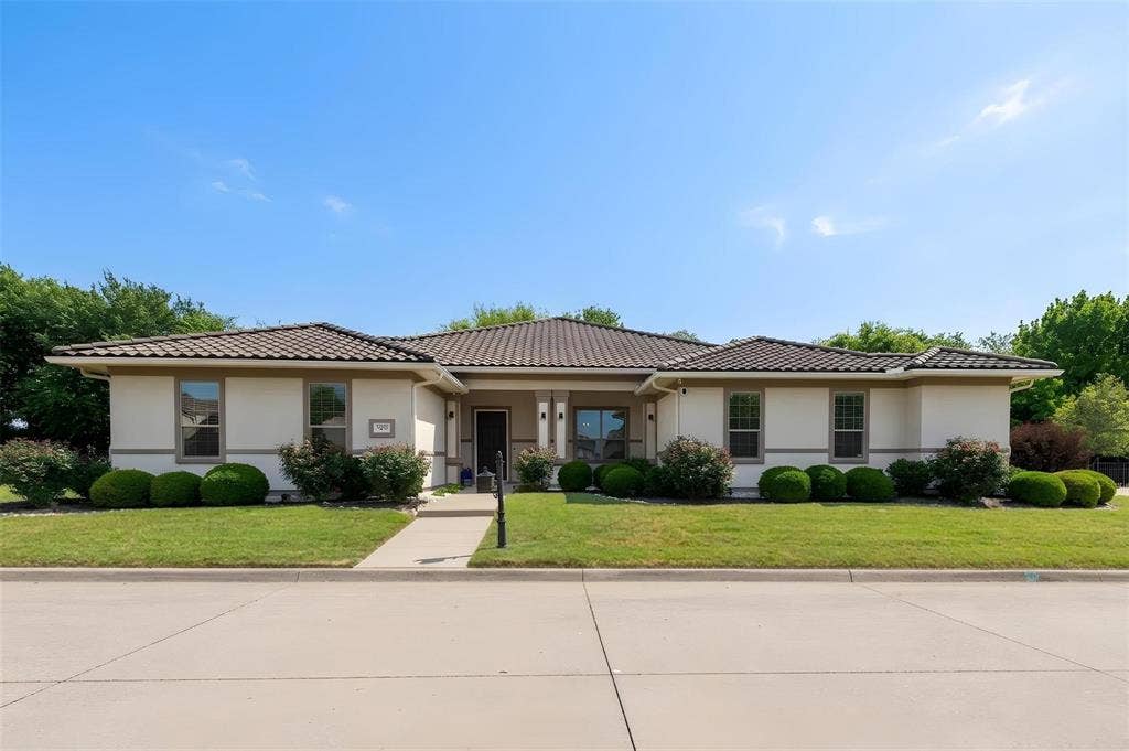 Stucco exterior with a tiled roof, concrete driveway, and a landscaped front yard with manicured shrubs