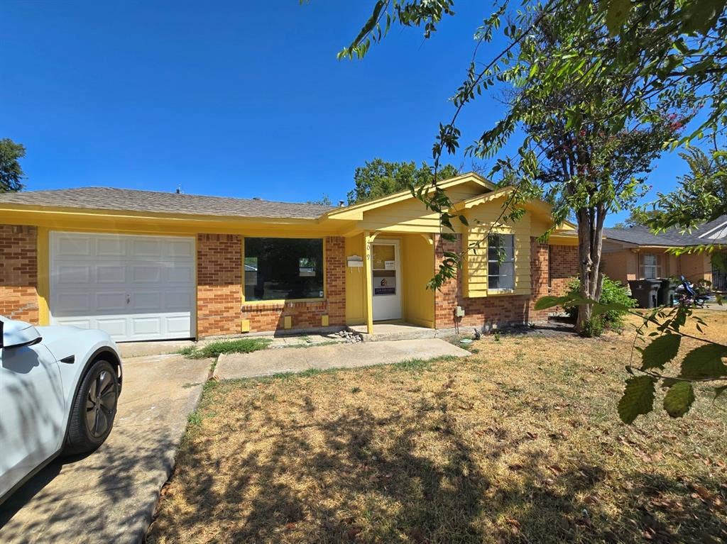 409 Monica Drive, Garland, TX 75041 Brick exterior with yellow siding accents, an attached garage, and a concrete driveway