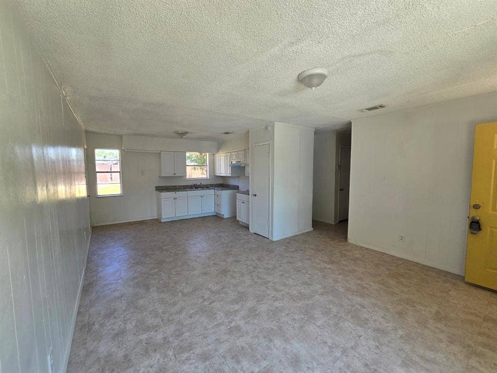 409 Monica Drive, Garland, TX 75041 Open-concept living area with vinyl plank flooring, a kitchen featuring white cabinetry and laminate countertops, and multiple windows providing natural light