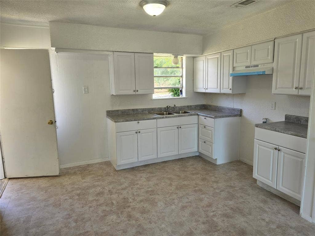 409 Monica Drive, Garland, TX 75041 Kitchen featuring white cabinetry, gray speckled countertops, a double basin stainless steel sink, and light-toned linoleum flooring