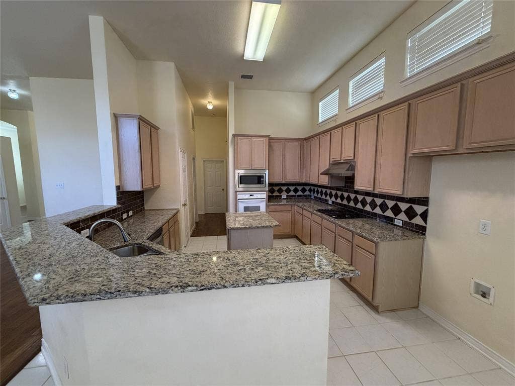 4413 Jenkins Drive, Plano, TX 75024 Kitchen featuring extensive light wood cabinetry, granite countertops, tile flooring, and a patterned tile backsplash