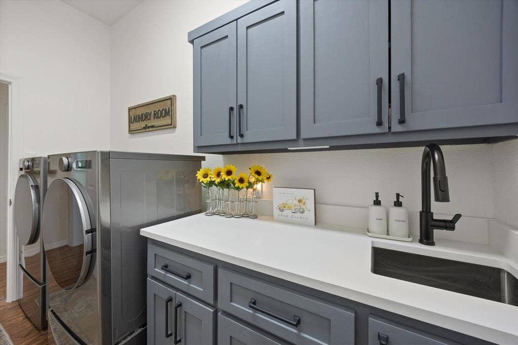 9604 Champions Drive, Granbury, TX 76049 Laundry Room Featuring Custom Upper and Lower Cabinets with Trash Drawer, New Quartz Countertops and Stainless-Steel Sink