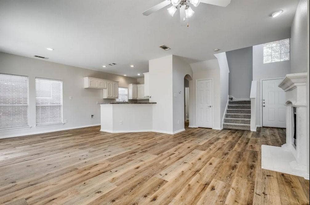 Wood-finish flooring throughout the main living space, kitchen island with counter seating, built-in fireplace, and staircase with carpeted treads